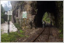 Pedestrains walking through a tunnel over the train tracks.  The sign reads "Prohibido el paso de patones por el tunel" ("The passage of pedestrians through the tunnel is prohibited.")