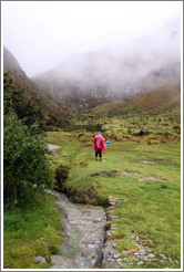 Man in a red rain poncho, looking at the mountains.