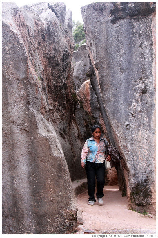 Woman walking between tall rocks, Qenko ruins.