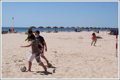 Kids playing soccer on the beach.