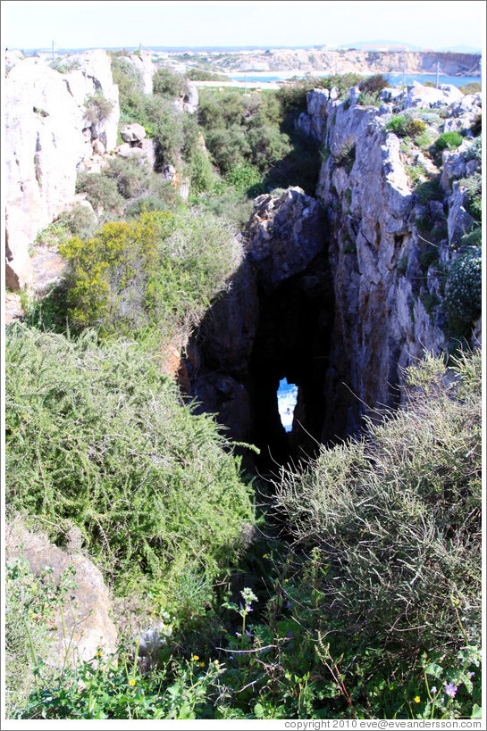 A cavern in a sea cliff, through which a little sea and rock can be seen.