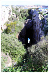 A cavern in a sea cliff, through which a little sea and rock can be seen.