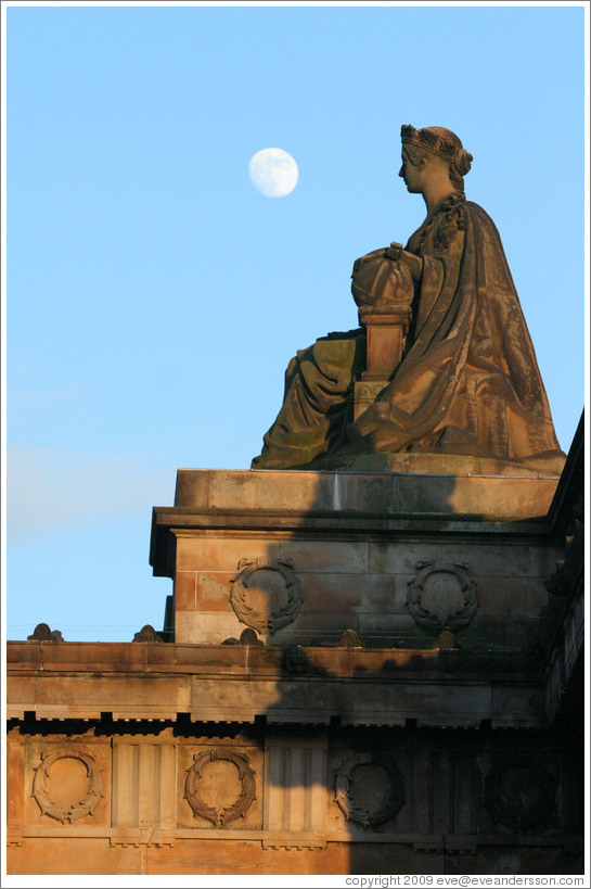 The moon appearing to hover near a statue of a woman atop the Royal Scottish Academy&#8206; building.