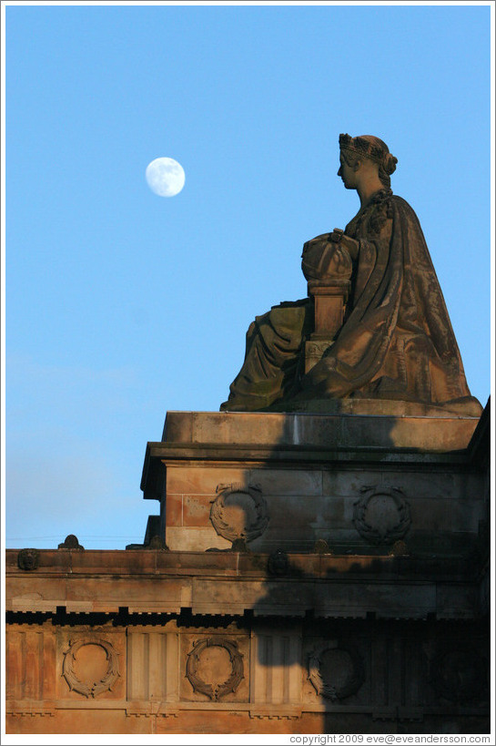 The moon appearing to hover near a statue of a woman atop the Royal Scottish Academy&#8206; building.