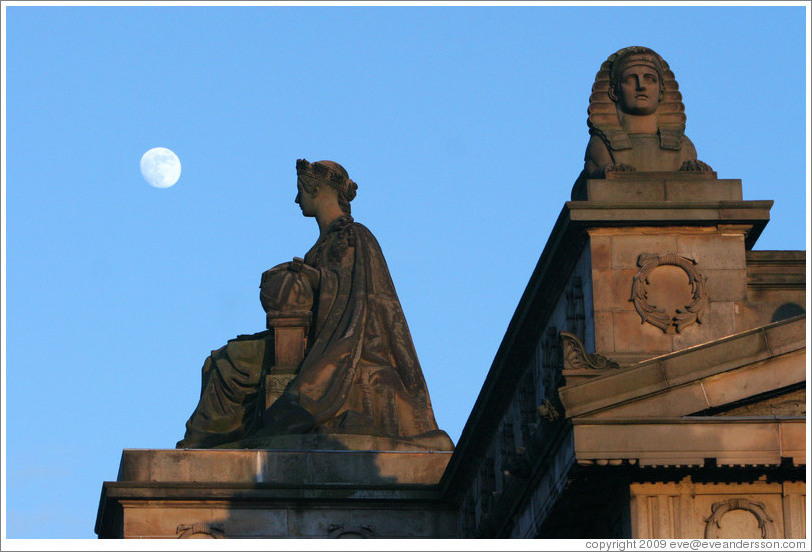 The moon appearing to hover near statues of a woman and a sphinx atop the Royal Scottish Academy&#8206; building.