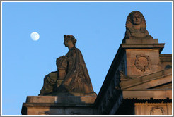 The moon appearing to hover near statues of a woman and a sphinx atop the Royal Scottish Academy&#8206; building.