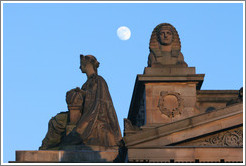 The moon appearing to hover near statues of a woman and a sphinx atop the Royal Scottish Academy&#8206; building.