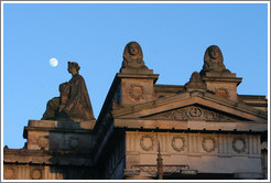 The moon appearing to hover near statues of a woman and sphinxes atop the Royal Scottish Academy&#8206; building.