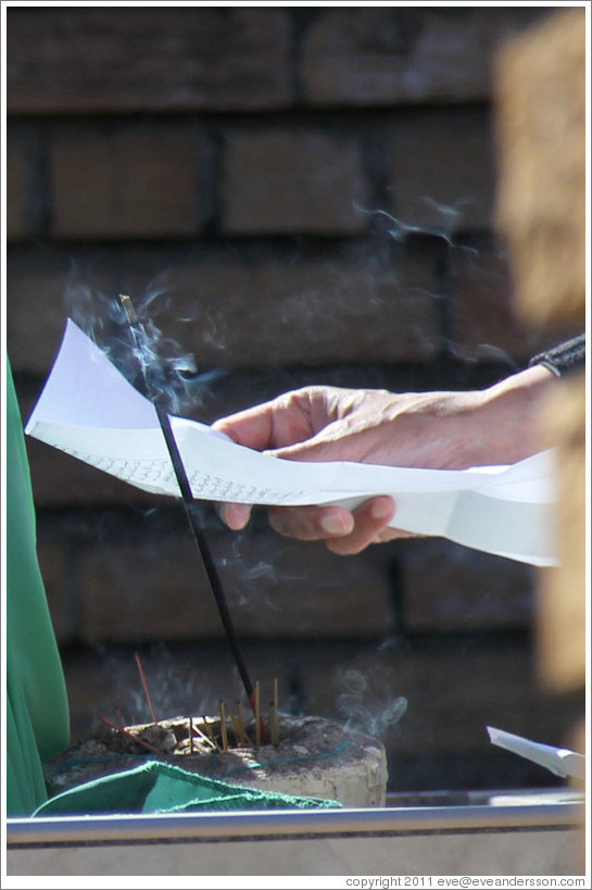 Hand holding a paper behind burning incense. Tana Baru cemetery, Bo-Kaap.