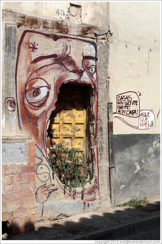 Graffiti. A face around an unused door says, "Casas sin gente / gente sin casa" ("Homes without people / people without homes"). Calle de San Juan de los Reyes, Albaic?