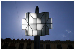 Street light during the day, with the sun above it.  Calle Gran V?de Col? City center.