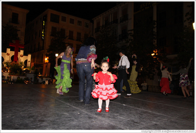 Girl in red among people dancing flamenco on the street at night during the Fiesta de las Cruces.  Plaza del Carmen.  City center.