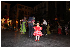 Girl in red among people dancing flamenco on the street at night during the Fiesta de las Cruces.  Plaza del Carmen.  City center.