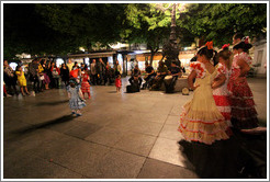 Three girls looking on street performers play music and others dance.  Fiesta de las Cruces.  Plaza de Bib-Rambla.  City center.