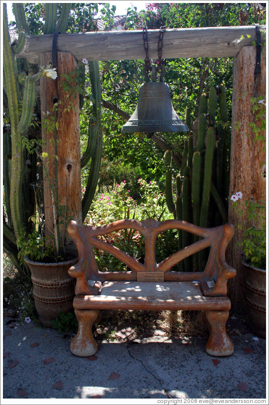 Bell and bench in garden.  San Juan Bautista Mission.