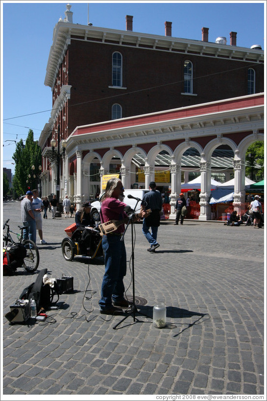 Street performer with one arm and two instruments.  Saturday Market.